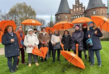 Eine Gruppe von Frauen steht mit orangenen Schirmen vor dem Holstentor.  - Copyright: Bastian Modrow