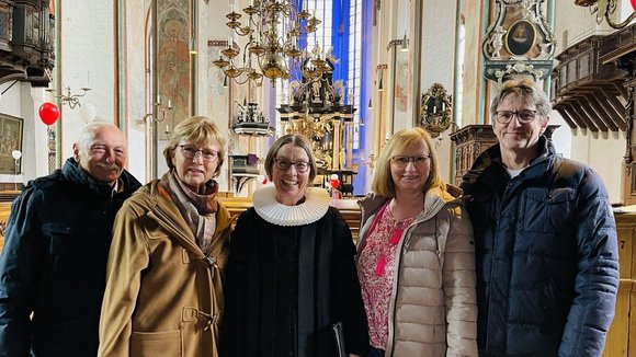 Eine Pastorin steht mit zwei Paaren in einer Kirche.