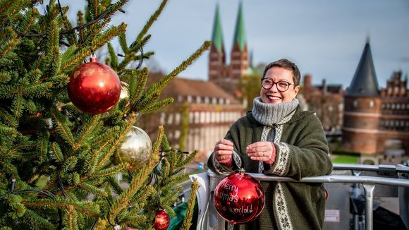 Eine Frau hängt eine Weihnachtsbaumkugel in einen Baum