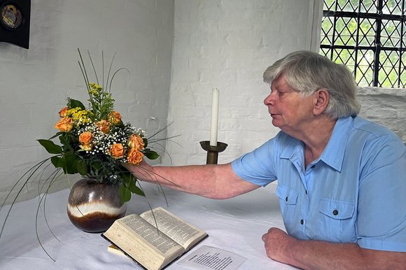 Eine Frau mit kurzen grauen Haaren beugt sich über einen Altar und ordnet einen Blumenstrauß.