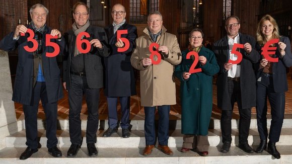 Sieben Menschen halten Ziffern in den Händen, die gemeinsam die Spendensumme ergeben