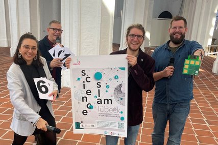 Vier Menschan halten in der St.-Petri-Kirche das Science-Slam-Plakat hoch. - Copyright: KKLL