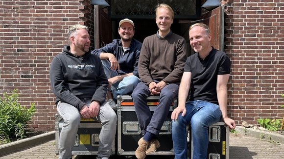 Vier Männer sitzen vor einer Kirche auf Technik-Containern.