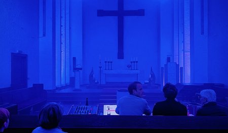 Ein blau erleuchteter Kirchenraum mit einem Kreuz.