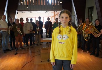 Ein Mädchen im Vordergrund, dahinter ein Posaunenchor in einer Kirche - Copyright: Tim Karweick