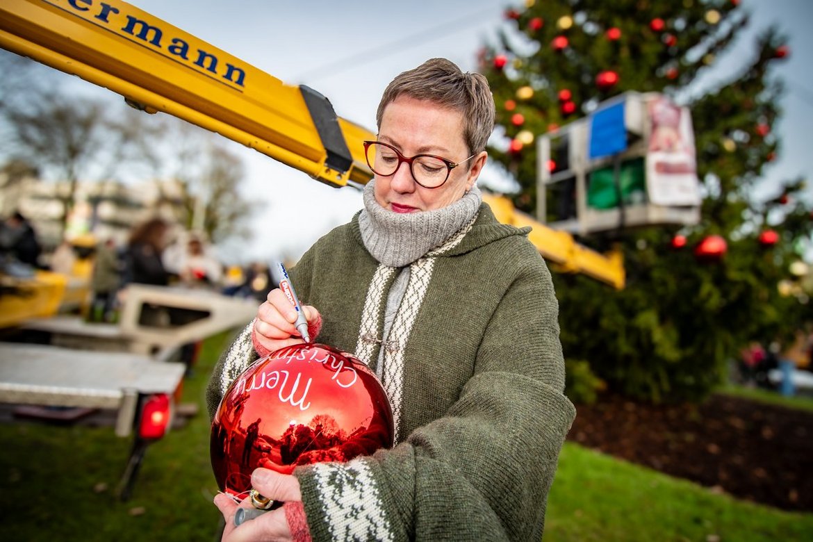 Eine Frau hängt eine Weihnachtsbaumkugel in einen Baum