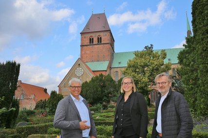 Zwei Männer und eine Frau stehen vor einem Kirchturm. - Copyright: Thomas Biller