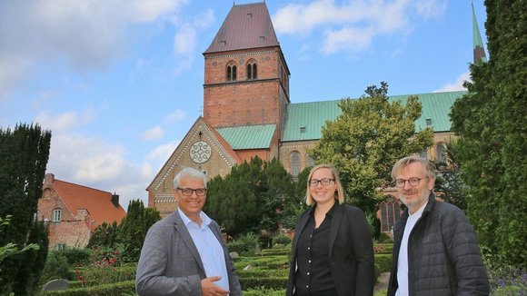 Zwei Männer und eine Frau stehen vor einem Kirchturm.