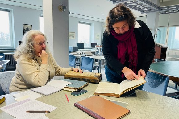 Zwei Frauen lesen im Archiv in alten Büchern.