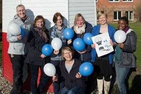 Mehrere Frauen stehen zusamen, halten Luftballons und lächeln.