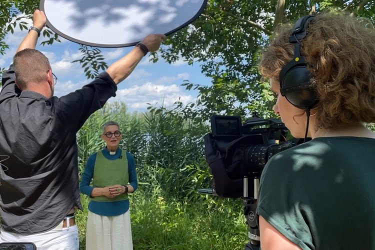 Pastorin Katja von Kiedrowski wird in einer üppigen Naturlandschaft gefilmt. Eine Kamera zeigt in ihre Richtung. - Copyright: Jule Klapproth