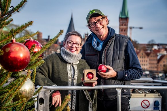 Eine Frau hängt eine Weihnachtsbaumkugel in einen Baum