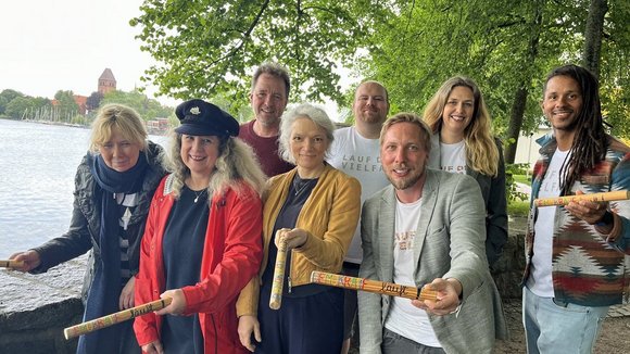 Mehrere Menschen stehen an einem See und halten Staffelstäbe in den Händen.