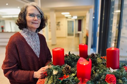 Frau steht lächelnd neben einem Adventskranz an dem vier Kerzen angezündet sind. - Copyright: Katharina Micheel