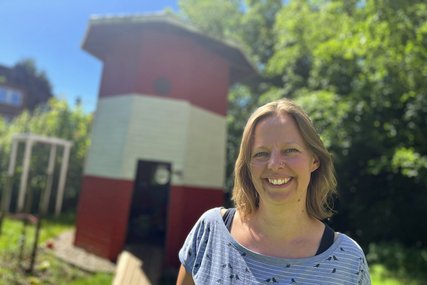 Eine Frau mit blonden Haaren steht vor einem Leuchtturm aus Holz in einem Garten. - Copyright: Annkathrin Bornholdt