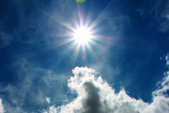 Die Sonne strahlt am Himmel, ein paar Wolken unterhalb der Sonne sind zu sehen