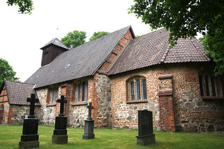 Drei Steinkreuze stehen vor der St.-Laurentius-Kirche auf grünem Rasen