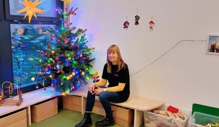 Eine Frau sitzt auf einer Holzbank vor einem geschmückten Weihnachtsbaum.