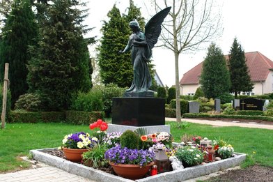 Engelfigur auf einem Sockel mit Blumen   - Copyright: Ev.-Luth. Kirchengemeinde Schwarzenbek