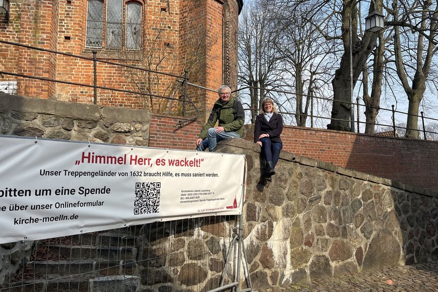 Alte Kirchenmauer mit einem Spendenbanner und zwei Personen, die auf der Mauer sitzen. - Copyright: Annkathrin Bornholdt