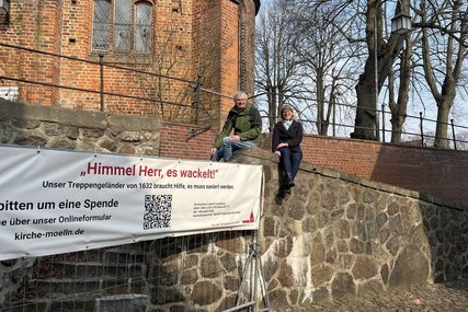 Alte Kirchenmauer mit einem Spendenbanner und zwei Personen, die auf der Mauer sitzen. - Copyright: Annkathrin Bornholdt